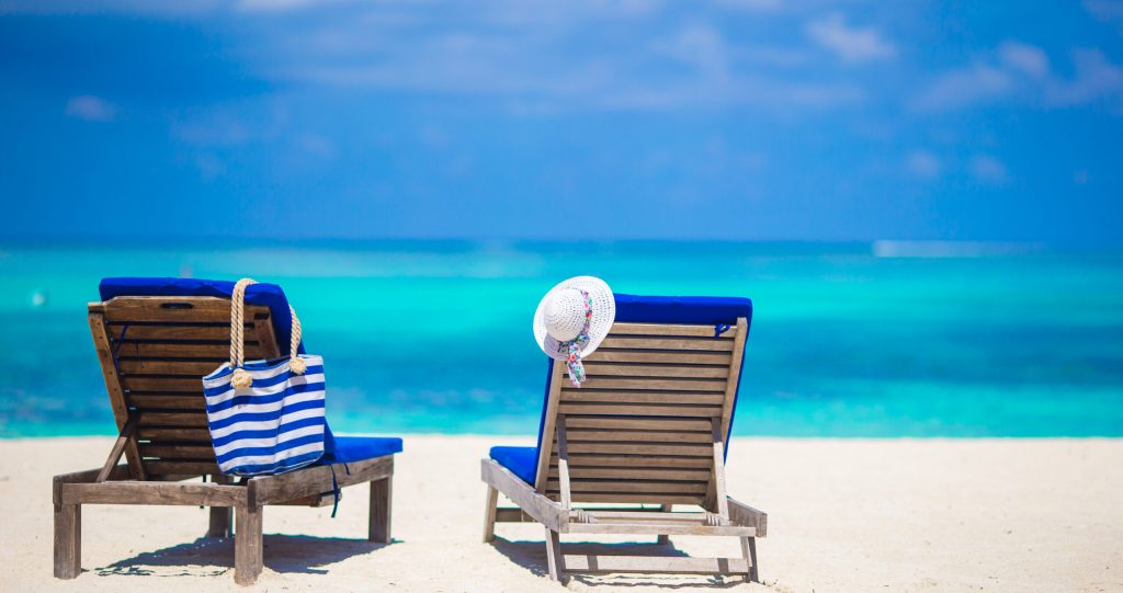 lounge chairs with bag and hat on tropical white beach